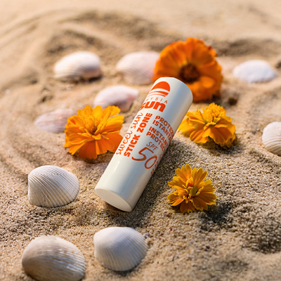 immagine del prodotto dello stick zone ambientato sulla sabbia circondato da fiori arancioni e gialli e conchiglie